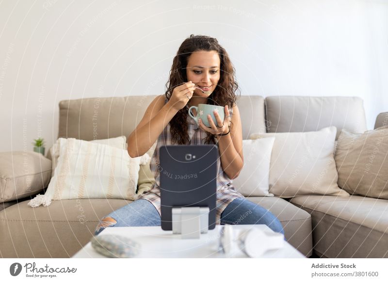 Woman drinking coffee and using tablet at home breakfast morning woman relax weekend watch movie entertain female outfit sofa cup gadget comfort domestic couch