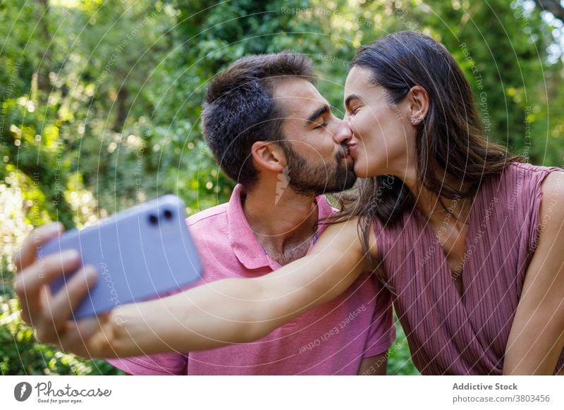 Cheerful ethnic couple taking selfie in park kiss happy smartphone cuddle date romantic love together relationship gadget mobile girlfriend boy young casual