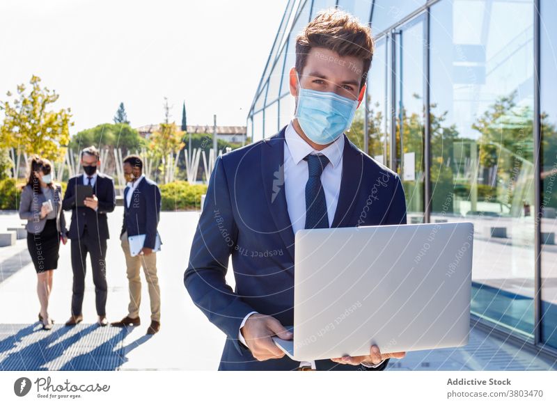 Focused businessman using laptop on street in sunlight work manager building new normal busy job colleague professional male young mask suit style diverse
