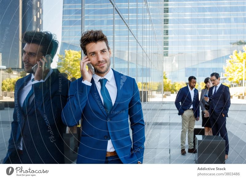 Delighted young businessman having phone conversation in downtown talk smartphone phone call happy smile style classy street city lean on building male