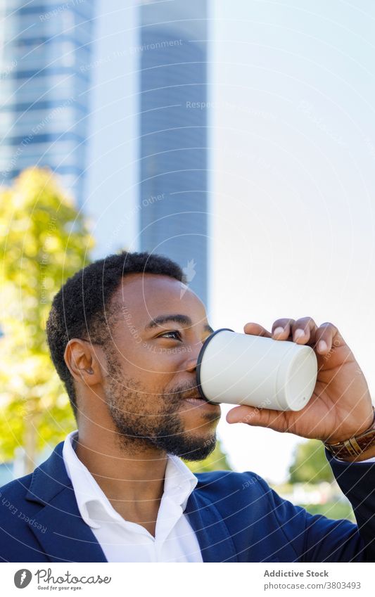 Bearded young black businessman drinking coffee in downtown street positive confident style beverage coffee break city sunlight urban male african american