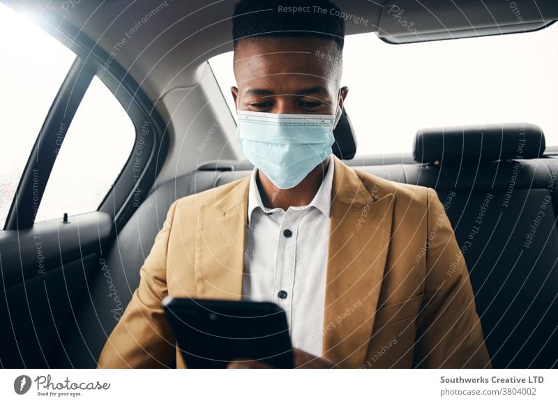 Young Businessman Wearing Mask Checking Mobile Phone In Back Of Taxi During Health Pandemic business businessman taxi face mask face covering wearing ppe cab
