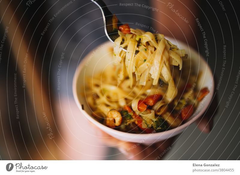 Hand uses fork to pickup tasty noodles with vegetables and shrimp on on dark background. Asian food concept. Top view. bowl chinese onion pasta dishes pepper
