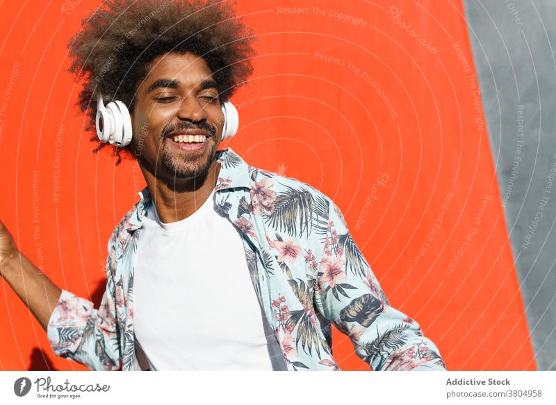 Stylish dreamy black man in modern headset on street headphones stylish listen music eyes closed masculine afro hairstyle african american ornament wear