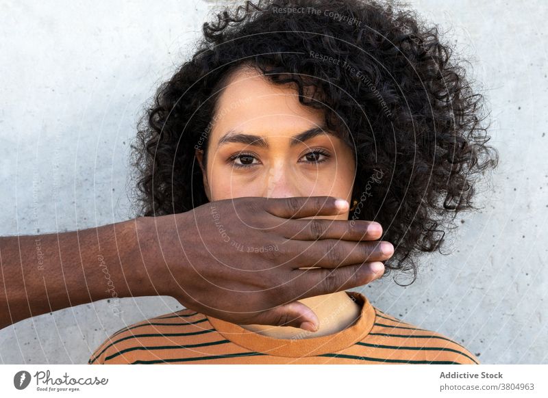 Crop black man covering mouth of unrecognizable ethnic woman cover mouth speechless mute hairstyle afro portrait unemotional individuality friend cover face
