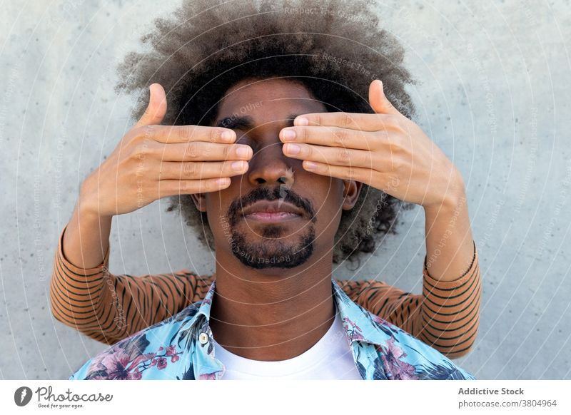 Anonymous partner covering eyes of black man near cement wall cover eyes friend focus stylish appearance afro hairstyle attentive portrait trendy modern casual