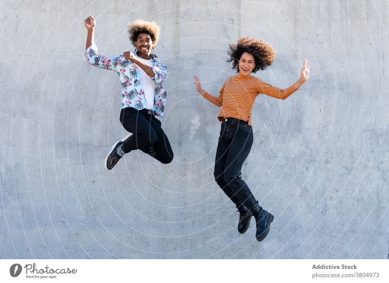 Excited diverse friends jumping near wall on street excited having fun stylish apparel happy afro hairstyle trendy multiracial couple friendship cement partner