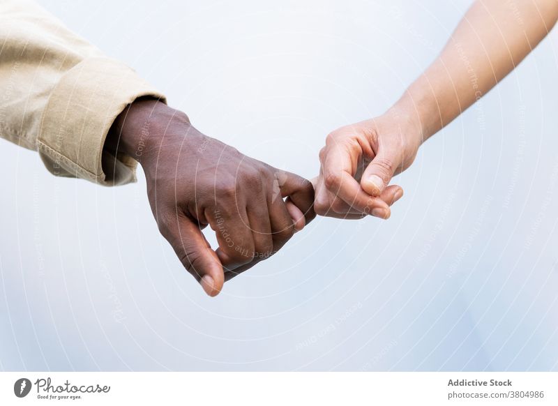 Crop multiracial couple holding little fingers holding hands pinky grip love relationship together gentle bonding care casual style boyfriend girlfriend