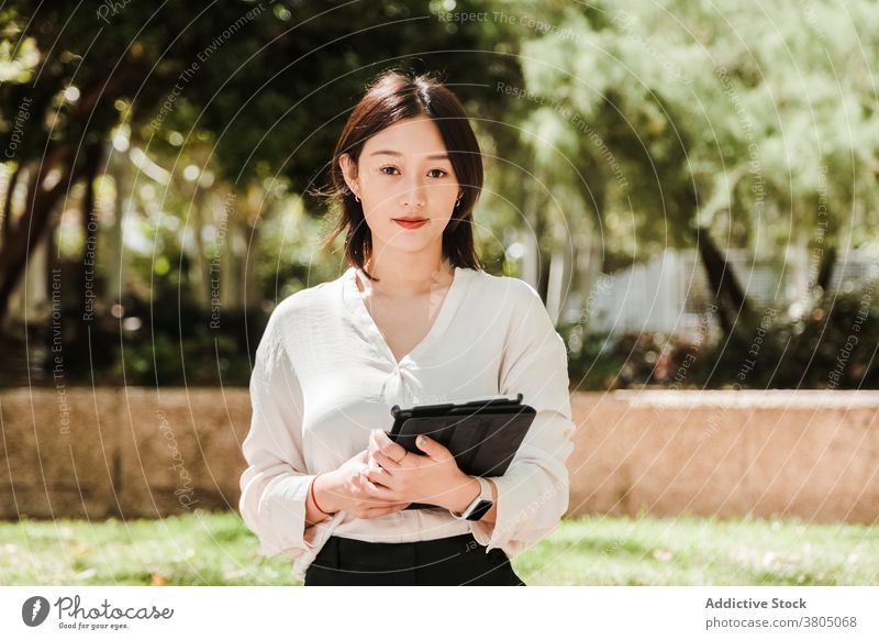 Smiling Asian businesswoman with tablet in park positive smile entrepreneur work job style confident professional female young ethnic asian formal device modern