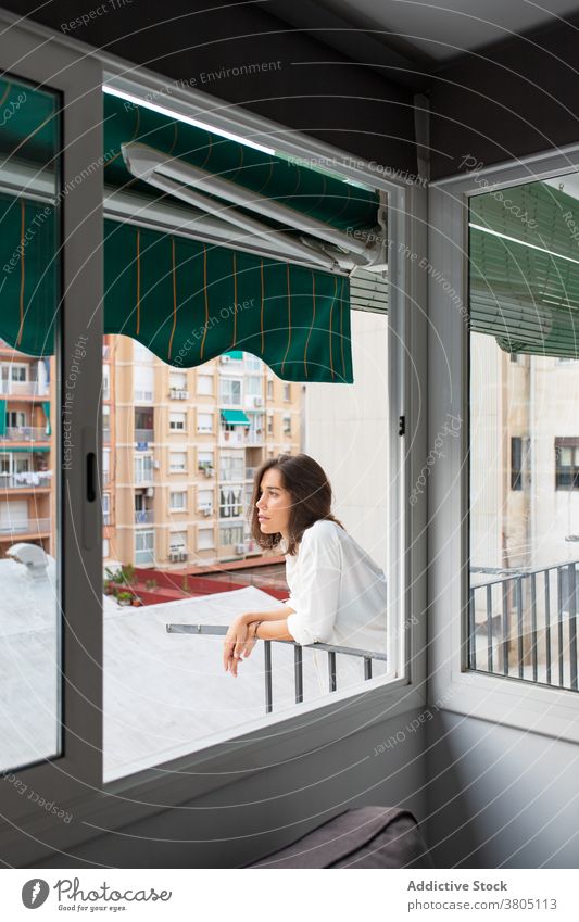 Calm young female on balcony of home woman morning calm enjoy relax rest terrace casual white shirt pensive dreamy recreation brunette sunlight peaceful