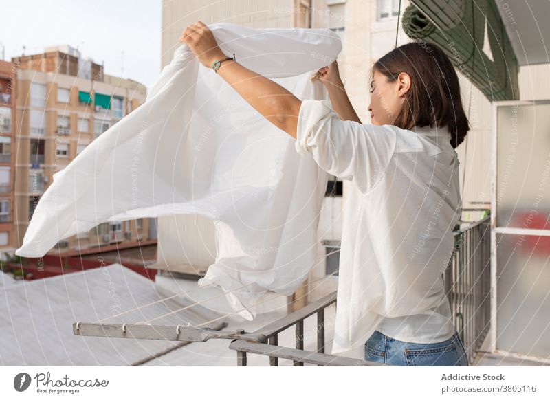 Young woman hanging laundry on balcony clothesline housework wash home bedsheet household hygiene routine female young white shirt jeans rope apartment casual