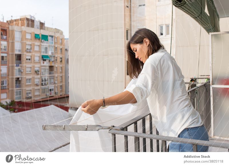 Young woman hanging laundry on balcony clothesline housework wash home bedsheet household hygiene routine female young white shirt jeans rope apartment casual