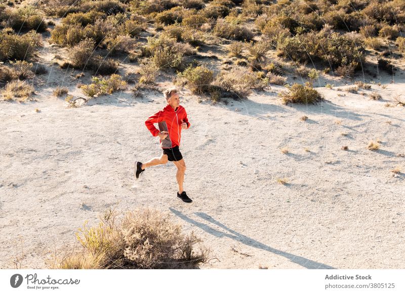 Sportsman jogging on sandy terrain in mountainous terrain run semi desert hill training active jogger healthy nature wellbeing exercise workout male activewear