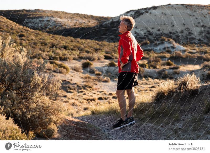 Sportsman resting on sandy terrain in mountainous terrain run semi desert hill training active healthy nature wellbeing exercise workout male activewear