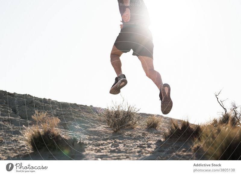 Unrecognizable man running in semi desert area on sunny day jump nature workout training energy sand active terrain runner male sportswear wellness healthy