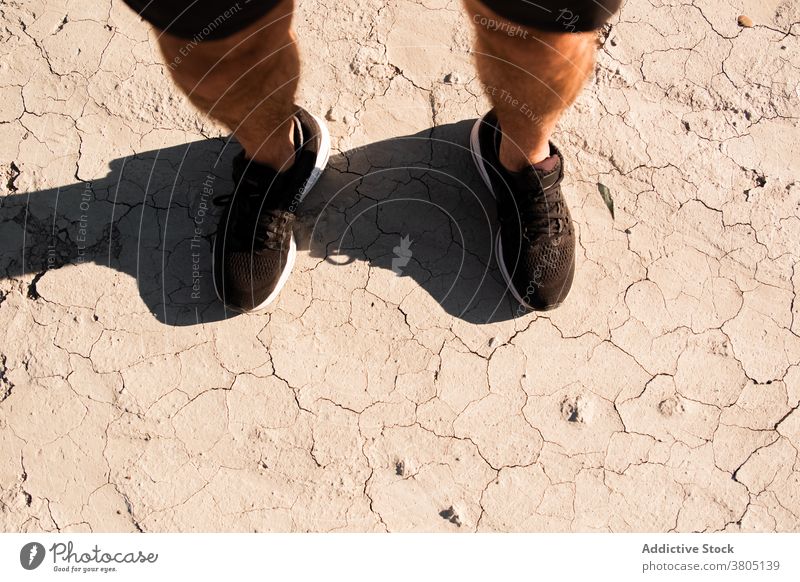 Anonymous guy in sporty shoes standing in desert after workout man arid ground training style rest recreation athlete exercise male sneakers shorts healthy leg