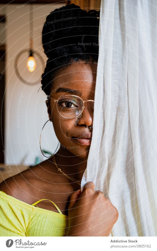 Stylish black lady hiding behind curtain at home woman cover face pensive calm trendy relax dreamy appearance serene confident female young african american