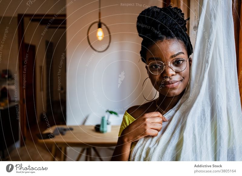 Stylish black lady hiding behind curtain at home woman cover face pensive calm trendy relax dreamy appearance serene confident female young african american