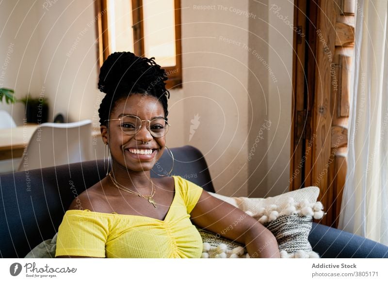 Cheerful black woman resting in living room toothy smile happy at home style fashion weekend free time sofa female african american eyeglasses apartment flat