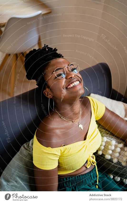 Cheerful black woman resting in living room toothy smile happy at home style fashion weekend free time sofa female african american eyeglasses apartment flat