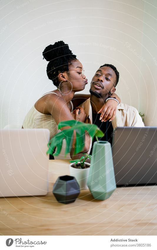 Cheerful black freelancers cuddling while having break couple relationship embrace at home laptop hug cuddle positive happy relax kiss african american plant