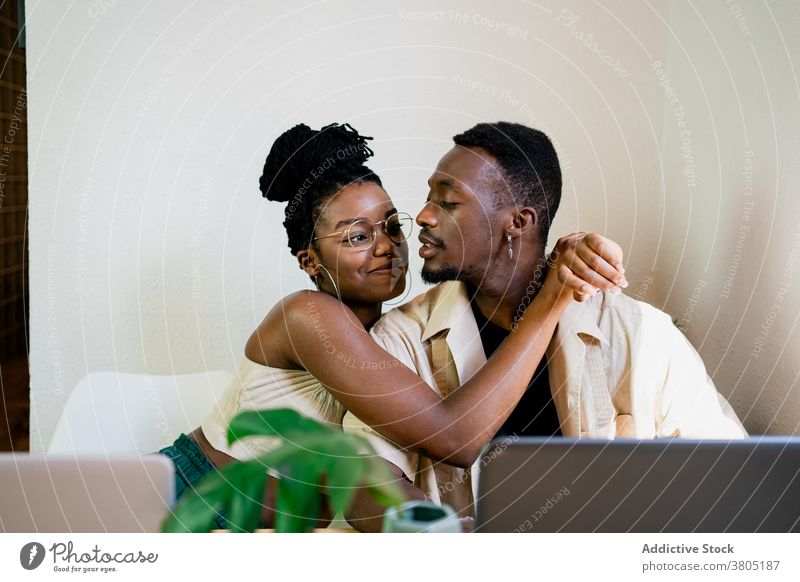 Cheerful black freelancers cuddling while having break couple relationship embrace at home laptop hug cuddle positive happy relax african american plant slim