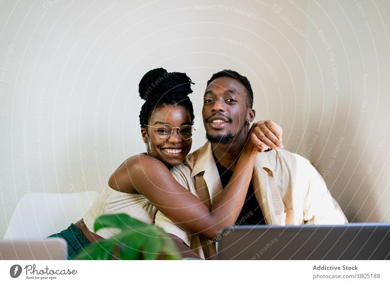 Cheerful black freelancers hugging while having break couple relationship embrace at home laptop cuddle positive happy relax african american plant slim wife