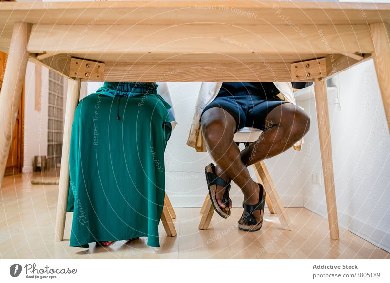 Faceless couple resting at wooden table man woman at home free time apartment together casual break african american black skirt shorts cloth apparel garment