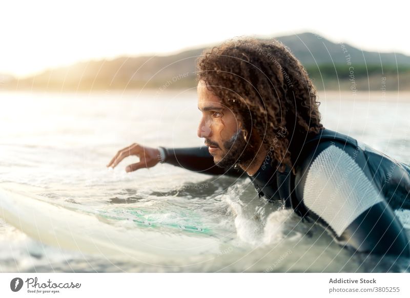Concentrated surfer looking at coming wave man sea ocean water sports summer focus leisure surfboard male serious pensive curly hair wetsuit vacation beach