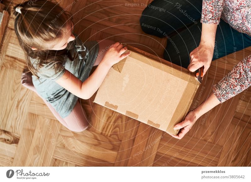 Woman unpacking a cardboard box parcel with help of her daughter view floor gift unboxing tape girl woman filler foam top open home wrapping opening shipping