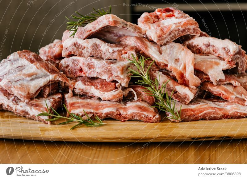 Pile of raw lamb ribs with fresh rosemary uncooked meat product fat organic protein pile aroma table wooden sprig aromatic herb bright heap edible natural