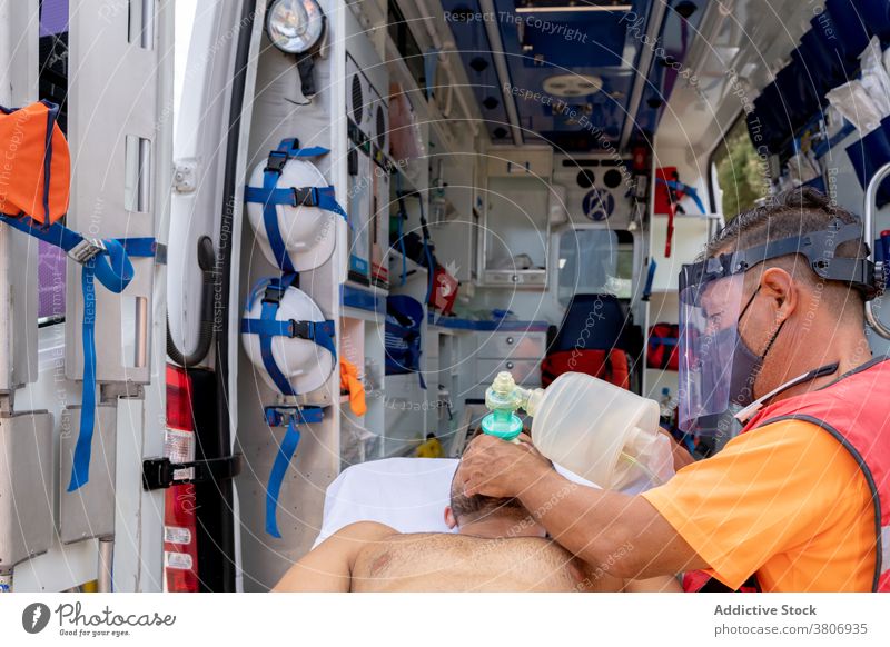 Unrecognizable lifeguard in visor putting oxygen mask on patient help medical aid profession ambulance emergency protective shield equipment uniform helmet