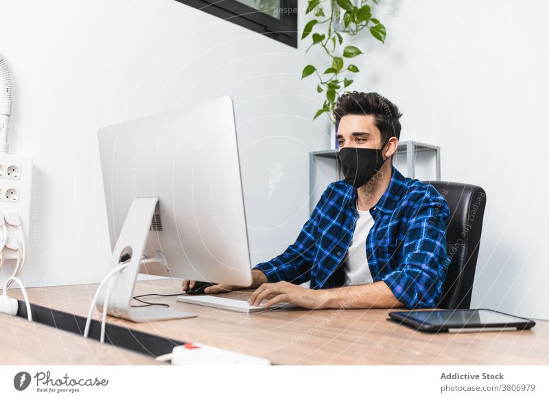 Anonymous businessman in mask typing on computer keyboard in office entrepreneur work project covid 19 concentrate desktop using device gadget tablet multimedia