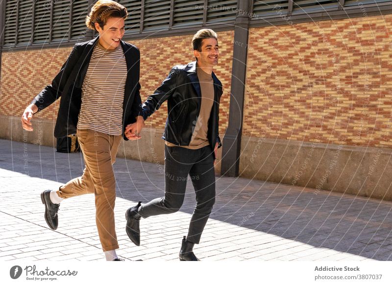 Happy stylish homosexual male couple running on city pavement gay holding hands relationship love apparel happy friend wall street same sex together affection