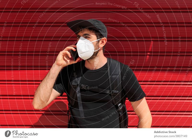 Man in mask speaking on smartphone on red background man covid 19 new normal phone call stylish apparel using gadget street wall ribbed trendy device quarantine