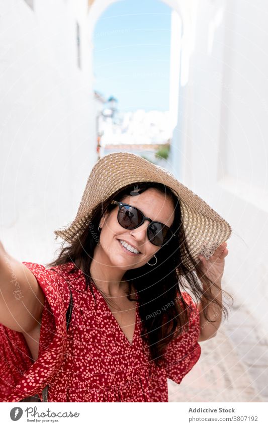 Happy tourist in sunglasses on narrow street in Greece building cheerful architecture style vacation summer white village rhodes island stylish woman straw hat