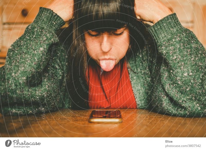 A young woman is annoyed and sticks her tongue out of her smartphone. Exasperated rabid Woman Cellphone technique digitization Online Dating harassment defiance