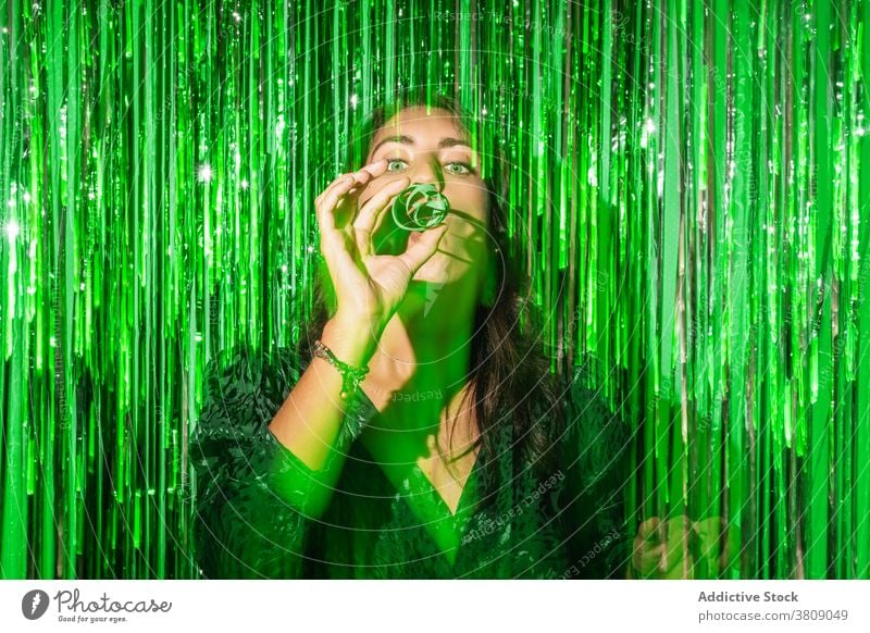 Content woman blowing party horn whistle green tinsel having fun sparkle glamour female outfit style happy vibrant vivid cheerful shiny trendy joy holiday