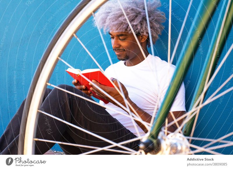Black and afro man reading a book next to his bicycle. Concept o black man reading red book afro black man afro hair biker cyclist student university student