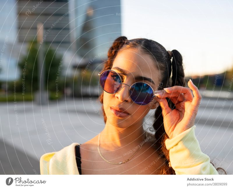 Cool young ethnic lady relaxing on the street woman training allure athlete trendy city sunglasses wellness female eyewear stylish fit hairstyle confident