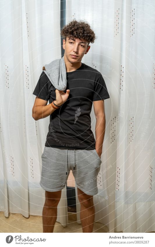 Attractive young man with curly hair wearing black t-shirt posing on white curtains background cheerful casual smile male adult handsome happy attractive