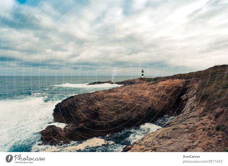 A wild lighthouse in the coast of the north of spains with giant rocks an wild waves crashing with copy space navigation guidance twilight beam safety sailing