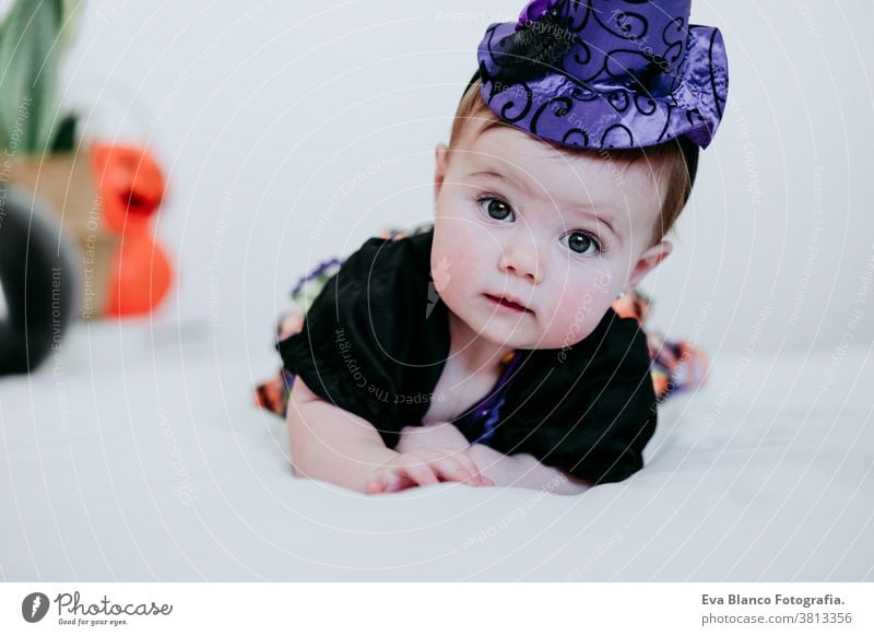 beautiful baby girl in witch halloween costume at home, sitting on bed with Halloween decoration, Lifestyle indoors trick or treat pumpkin balloons orange