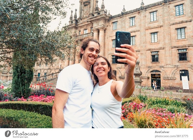Young couple taking a fancy selfie in a garden in front of an old building holiday happy smart-phone vacation brunette man outdoors kissing picture male