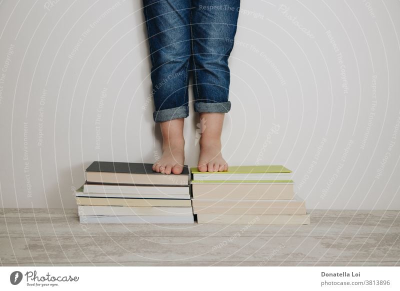child standing on stacks of books barefoot casual dress caucasian childhood concept education educational feet fun grow home homework indoors isolated jeans kid