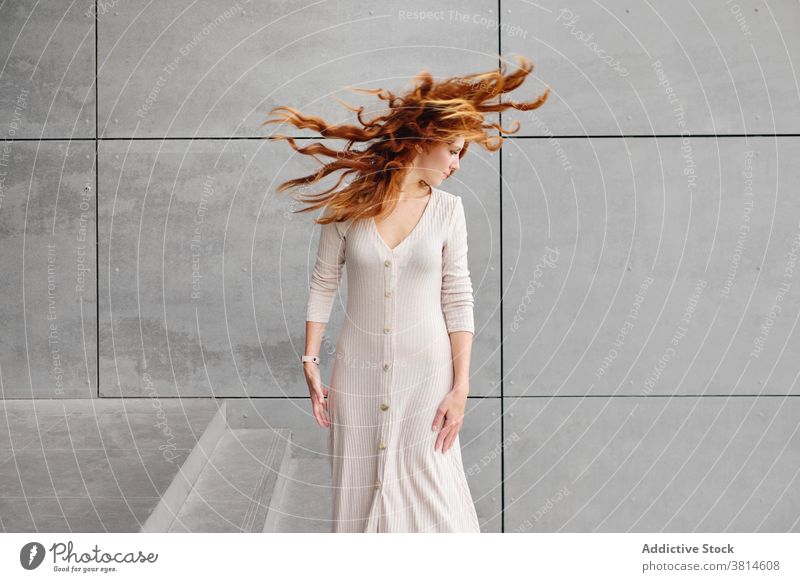 Ginger woman with flying hair standing near wall redhead ginger wind urban style long hair modern female red hair trendy color mystery contemporary elegant