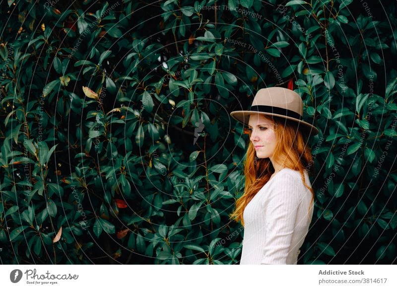 Young woman in hat standing in garden style redhead trendy red hair modern ginger vogue young female fashion long hair confident charming lifestyle elegant