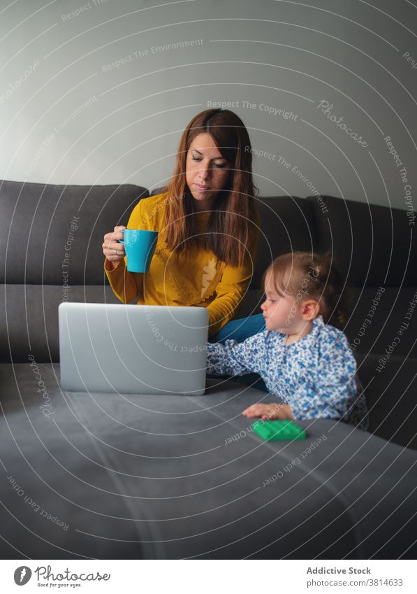 Businesswoman with little child working on laptop at home mother kid using coffee drink busy remote businesswoman online freelance toddler daughter together