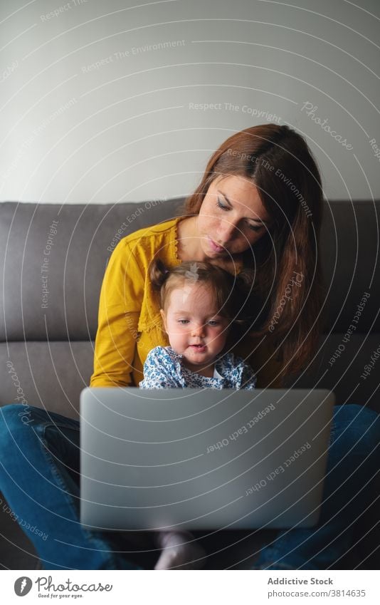 Woman with little kid using laptop at home mother work busy toddler remote daughter child together motherhood gadget device lifestyle mom browsing freelance