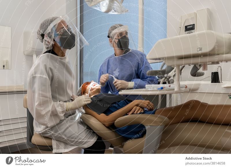 Dentists in protective face shields treating patient in clinic dentist dentistry stomatology equipment scan examine tool mask coronavirus pandemic safety